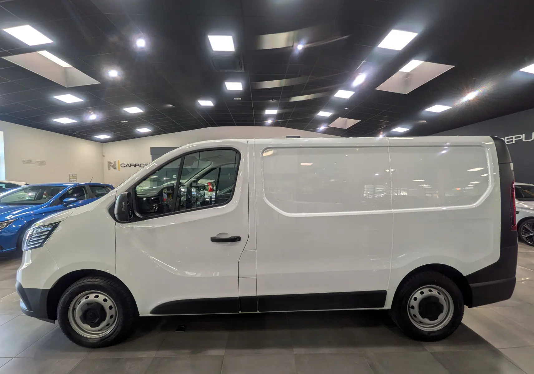 Vue de profil côté gauche d’un Renault Trafic Fourgon blanc minéral 2024 en intérieur, avec jantes acier et poignées noires.