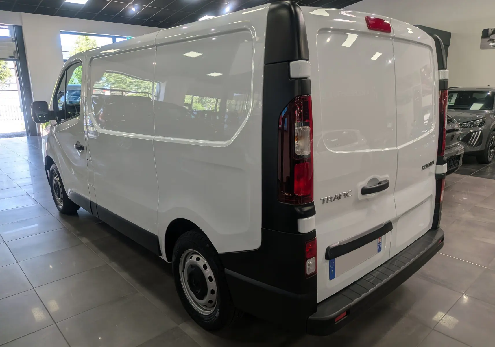 Vue 3/4 arrière droite du Renault Trafic Fourgon blanc minéral 2024 avec feux arrière verticaux et pare-chocs noir.