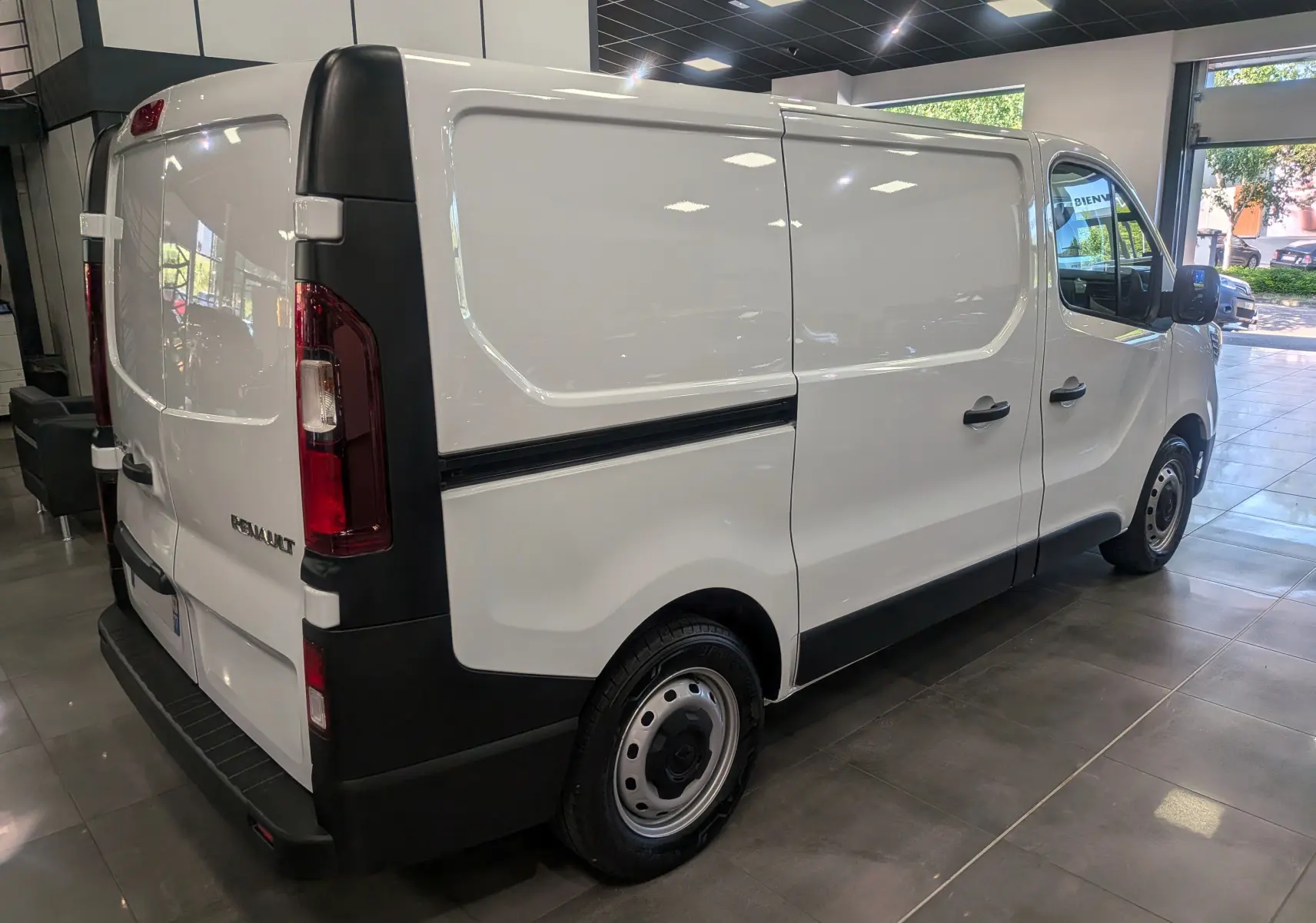 Renault Trafic Fourgon blanc minéral vu en 3/4 arrière droit, avec portes latérales et arrière fermées en intérieur showroom.