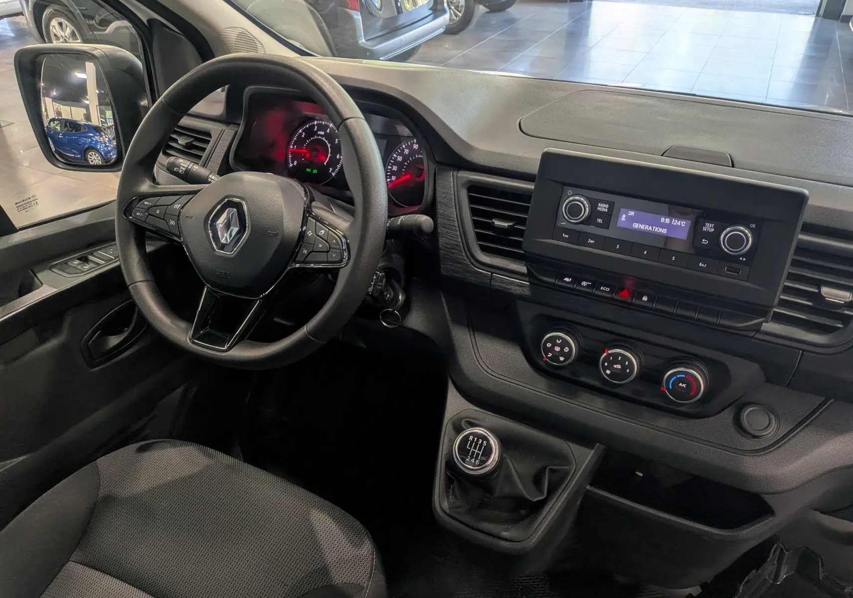 Vue intérieure côté conducteur du Renault Trafic Fourgon blanc, montrant le volant multifonction, tableau de bord et levier de vitesses manuel.