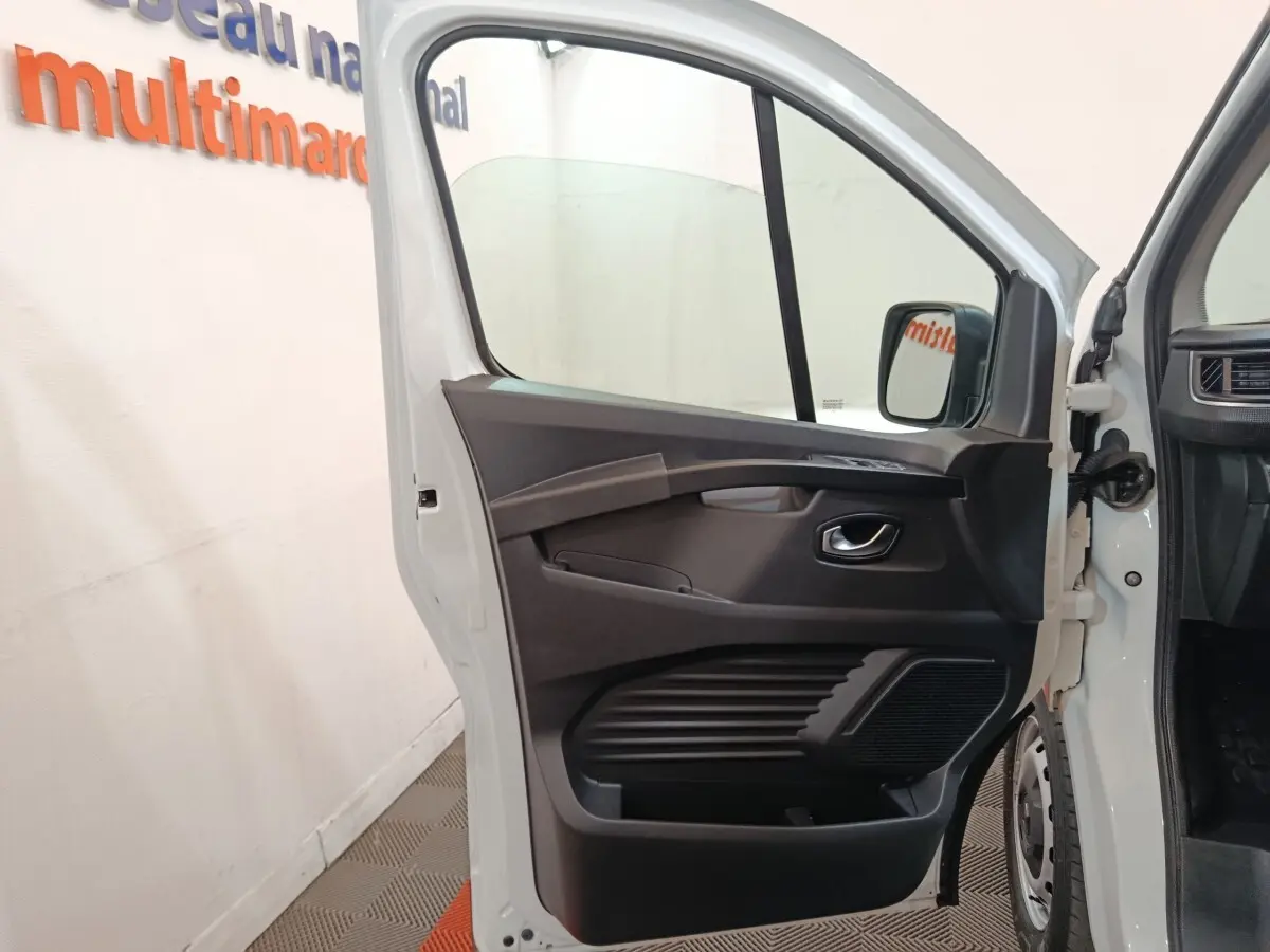 Vue rapprochée de la porte avant gauche ouverte d’un Renault Trafic blanc, montrant la garniture intérieure noire.