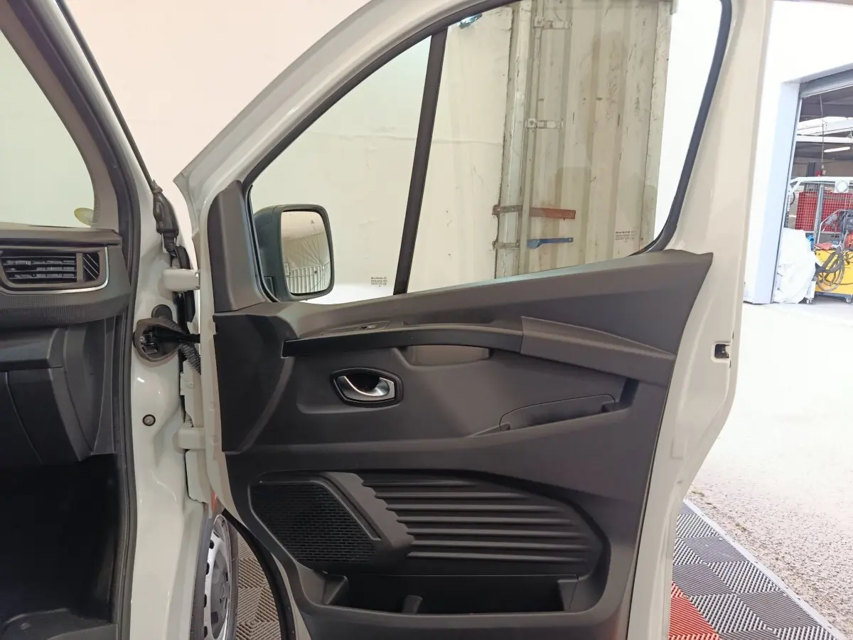 Vue intérieure de la porte avant gauche ouverte d’un Renault Trafic Fourgon blanc, avec panneau noir et poignée intégrée.