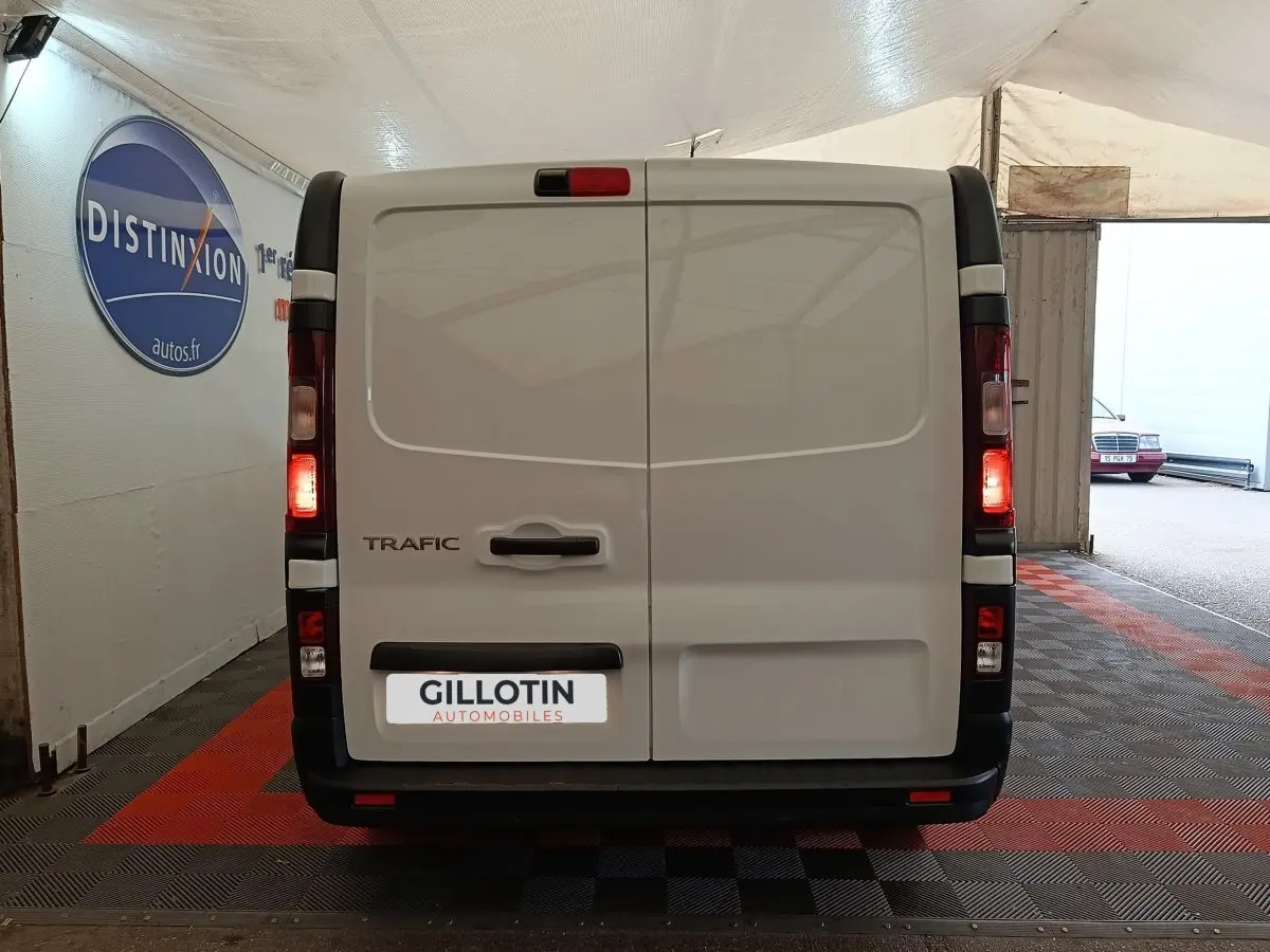 Vue arrière d’un Renault Trafic Fourgon blanc 2023 avec feux allumés dans un garage couvert.