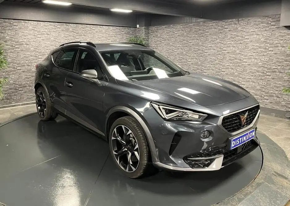Vue 3/4 avant droit d'une CUPRA Formentor gris magnétique avec jantes noires et détails chromés, en intérieur showroom.