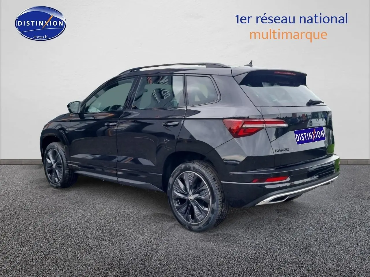 SKODA KAROQ noir 2025 en 3/4 arrière droit, avec jantes alu et barres de toit visibles.