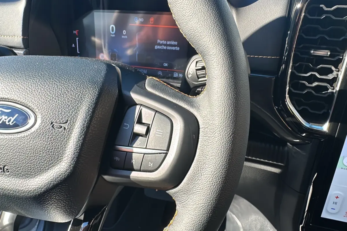 Gros plan sur le volant cuir multifonctions du Ford Ranger 2025, avec tableau de bord numérique en arrière-plan.