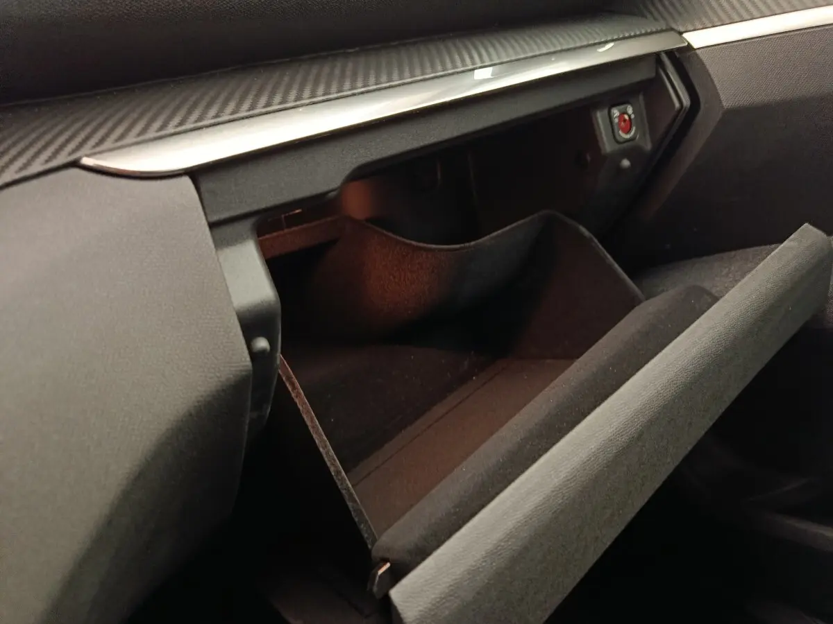 Gros plan sur la boîte à gants ouverte côté passager du Peugeot 5008 gris foncé, intérieur noir et détails en carbone.