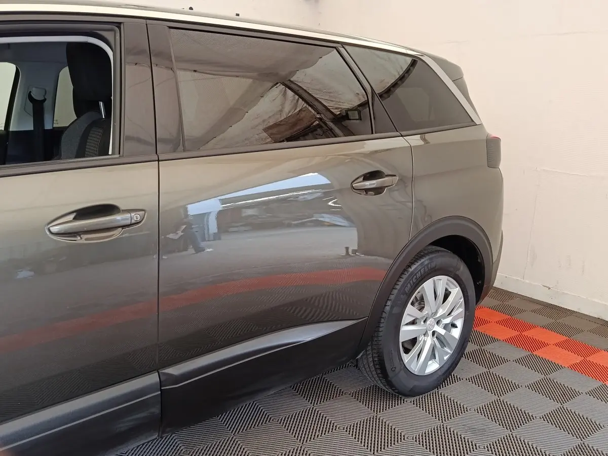 Vue latérale droite du Peugeot 5008 gris foncé, mettant en valeur les portes arrière et la roue arrière sur sol à damier.