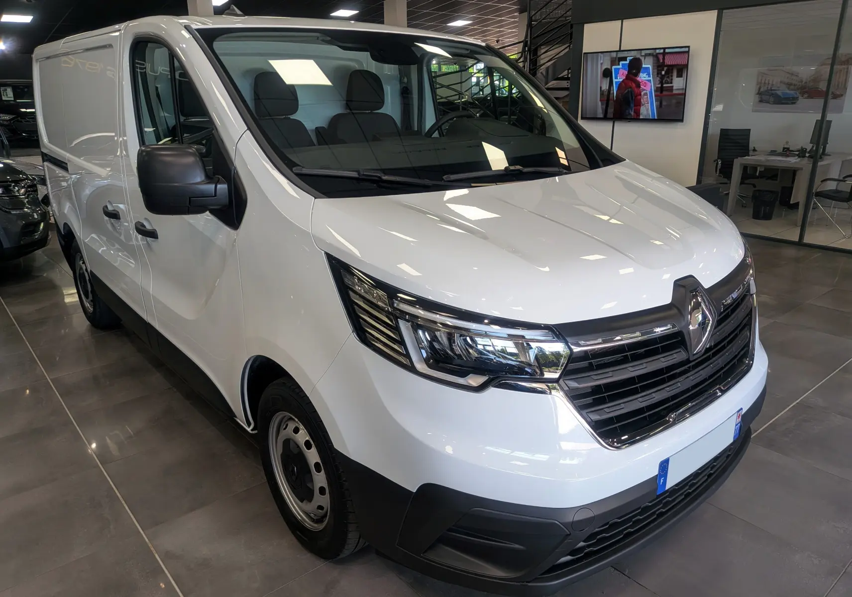 Vue 3/4 avant gauche d’un Renault Trafic Fourgon blanc minéral 2024 avec calandre noire et phares modernes.