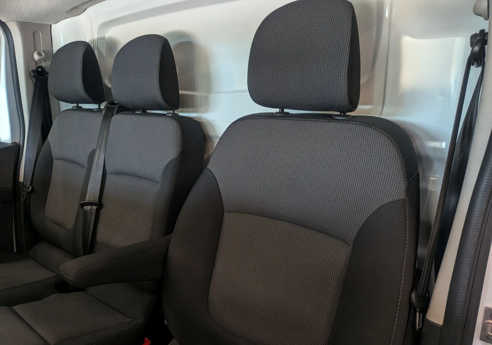 Vue intérieure des sièges avant en tissu gris foncé du Renault Trafic Fourgon 2024, avec cloison métallique blanche en arrière-plan.