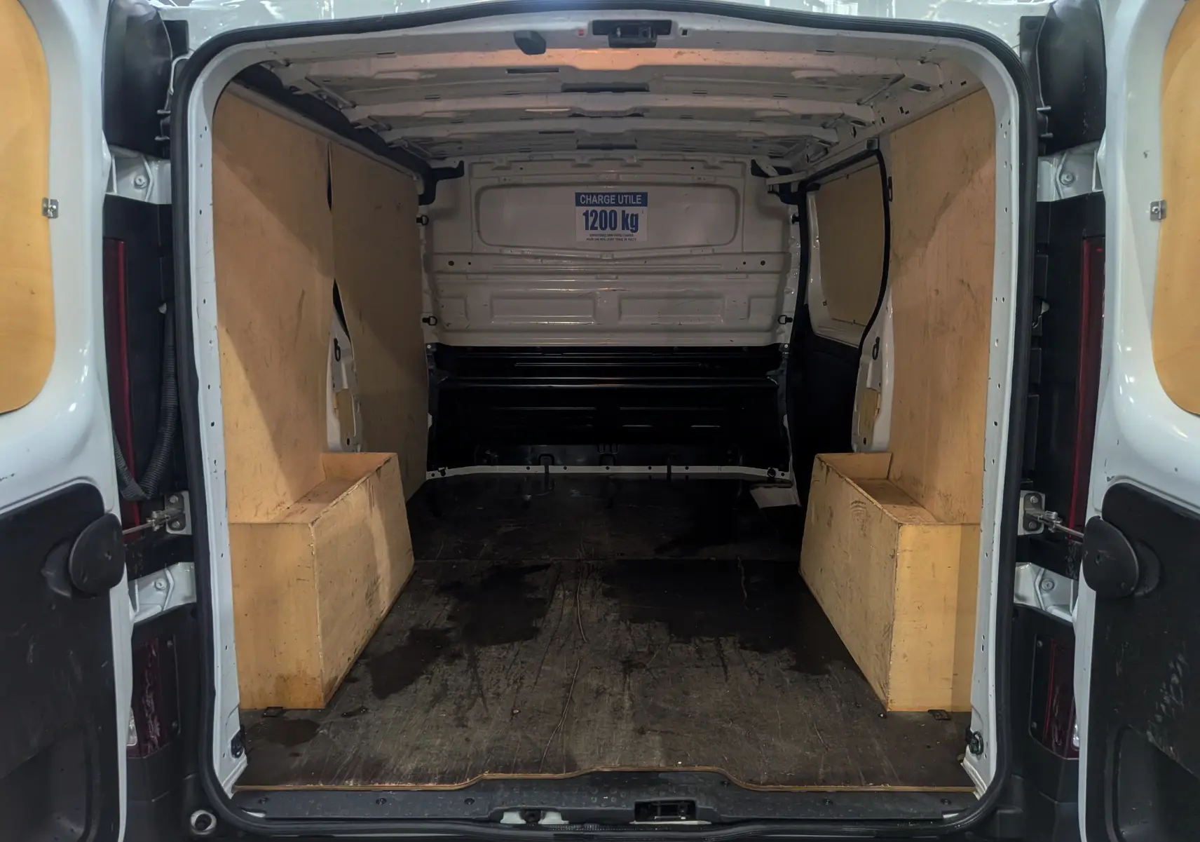 Intérieur du coffre du Renault Trafic Fourgon blanc minéral, vue arrière ouverte montrant l'espace de chargement avec panneaux en bois.