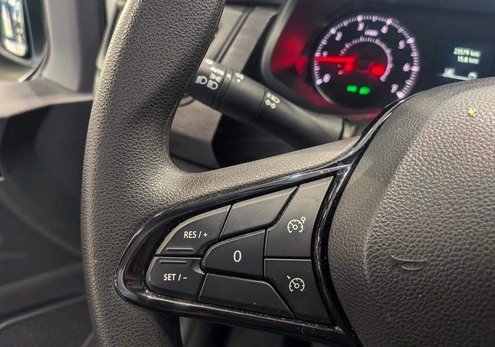 Gros plan sur les commandes de régulateur de vitesse au volant noir du Renault Trafic Fourgon 2024, tableau de bord en arrière-plan.
