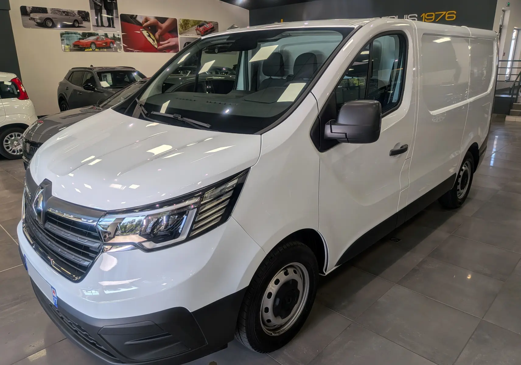 Vue 3/4 avant droite du Renault Trafic Fourgon blanc minéral 2024 avec calandre chromée et phares LED en showroom.