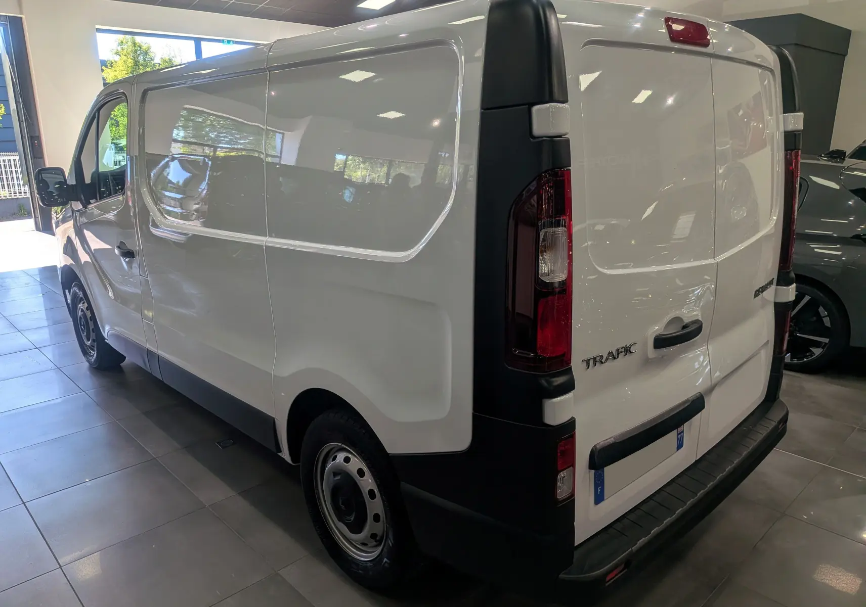 Vue 3/4 arrière droite d’un Renault Trafic Fourgon blanc minéral 2024, avec portes arrière fermées et jantes acier noires.