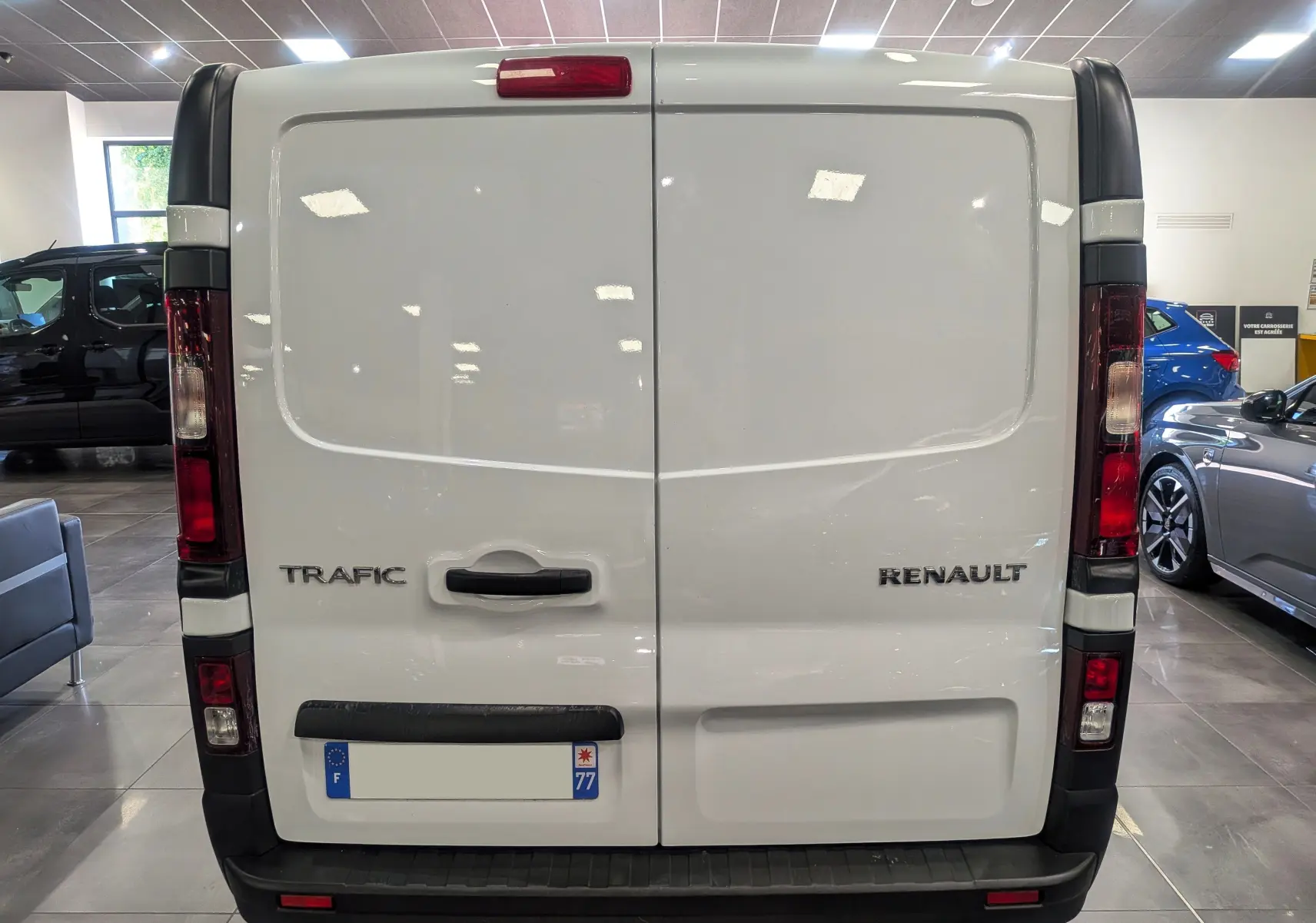 Vue arrière d’un Renault Trafic Fourgon blanc minéral 2024, portes battantes fermées avec logo et plaque d’immatriculation visible.