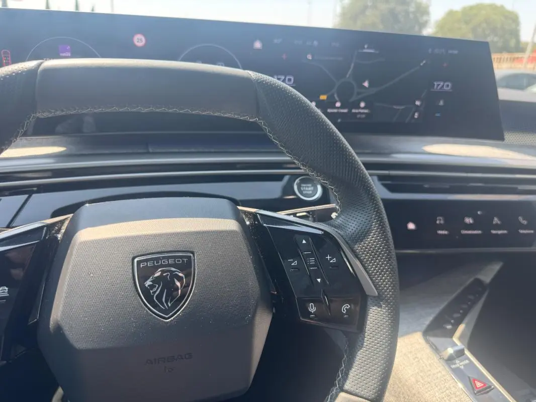 Vue intérieure centrée sur le volant noir perforé du Peugeot 3008 Hybrid 145 e-DCS6 GT avec cockpit numérique en arrière-plan.