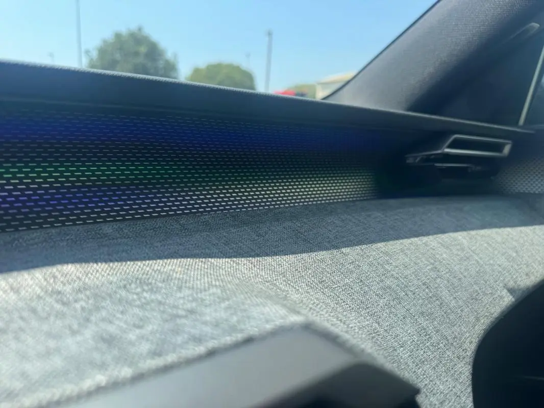 Détail de la planche de bord avec habillage tissu gris et bandeau lumineux dans un Peugeot 3008 Hybrid 145 e-DCS6 GT noir.