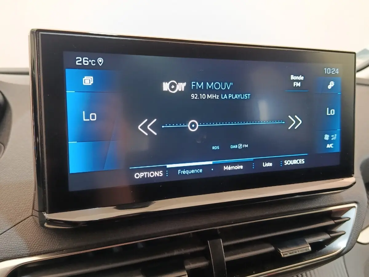 Gros plan sur l'écran tactile central du Peugeot 3008 noir, affichant la radio FM et la température intérieure à 26°C.