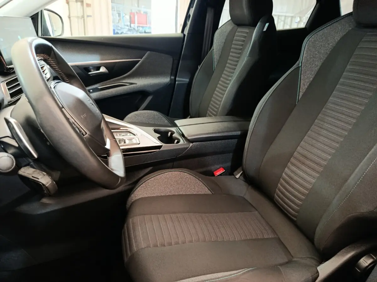 Vue intérieure côté conducteur du Peugeot 3008 noir, mettant en valeur les sièges en tissu et le volant cuir multifonctions.