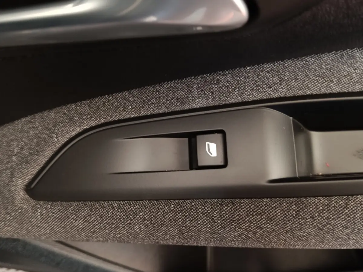 Gros plan sur le bouton de commande de lève-vitre intégré dans la garniture tissu gris côté porte d’un Peugeot 3008 noir 2022.
