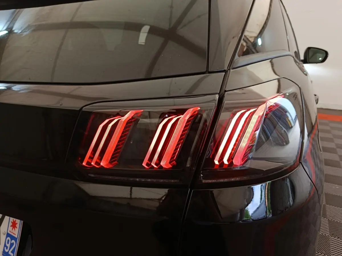 Feu arrière droit allumé du Peugeot 3008 noir, vue rapprochée du coin arrière en intérieur.
