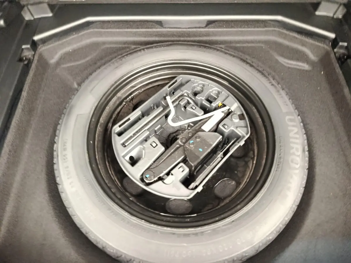 Vue plongeante sur la roue de secours noire et son kit d'outils dans le coffre du Peugeot 3008 noir 2022.