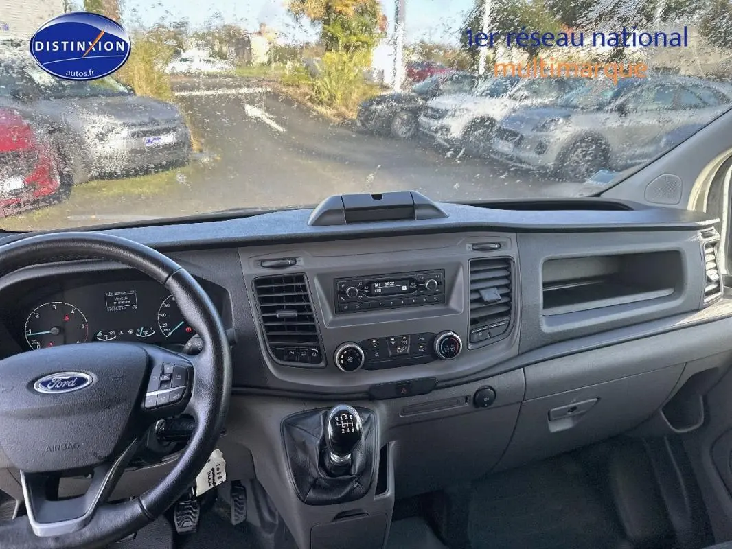 Vue intérieure du tableau de bord du Ford Transit Custom blanc, avec volant cuir et levier de vitesse manuel visible.