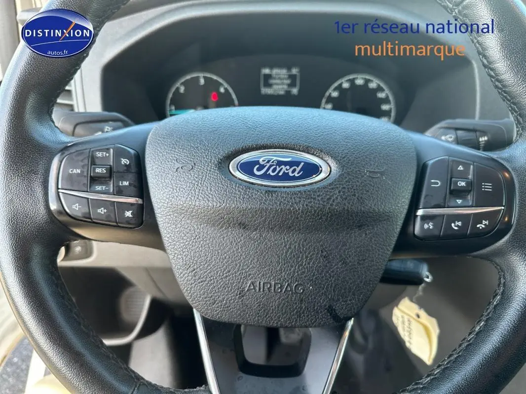 Volant cuir noir Ford avec commandes intégrées, tableau de bord partiellement visible en arrière-plan.