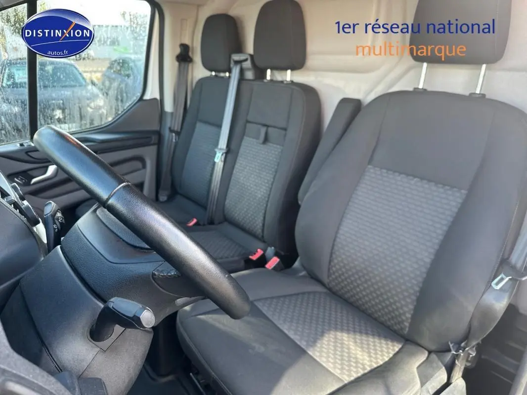 Intérieur du Ford Transit Custom blanc 2021, vue côté conducteur sur les sièges avant en tissu gris et volant cuir.