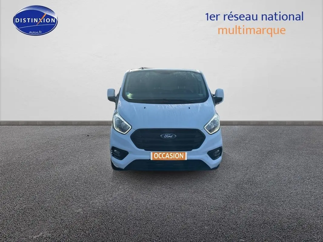 Vue frontale d'un fourgon Ford Transit Custom blanc avec calandre noire et plaque "OCCASION" orange visible.
