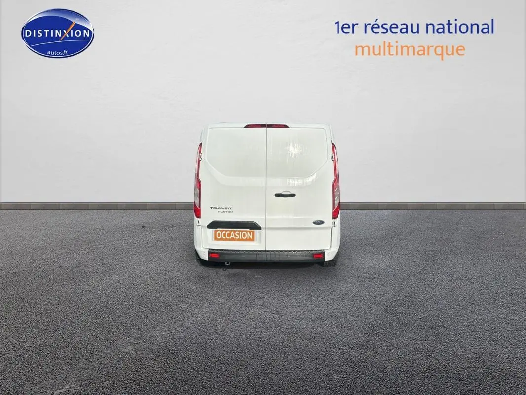 Vue arrière d'un fourgon Ford Transit Custom blanc avec portes battantes et plaque occasion visible.