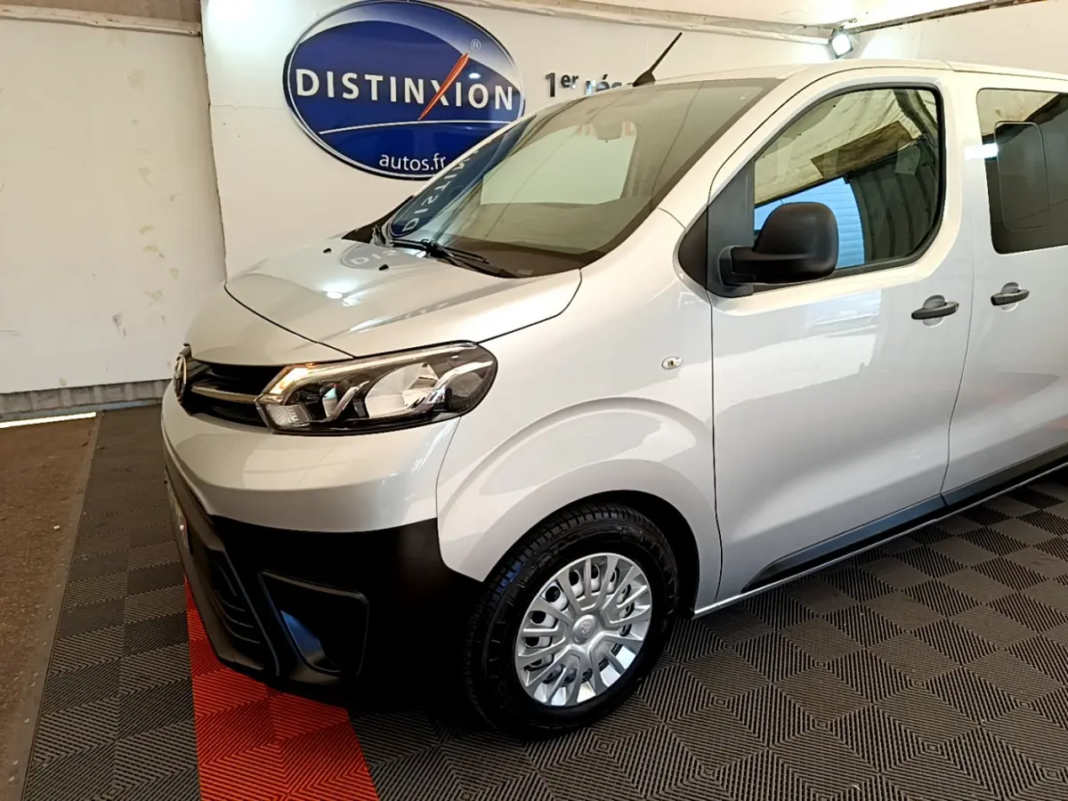 Vue 3/4 avant droit d'un Toyota Proace Verso gris clair avec pare-chocs noir et jantes acier en showroom.
