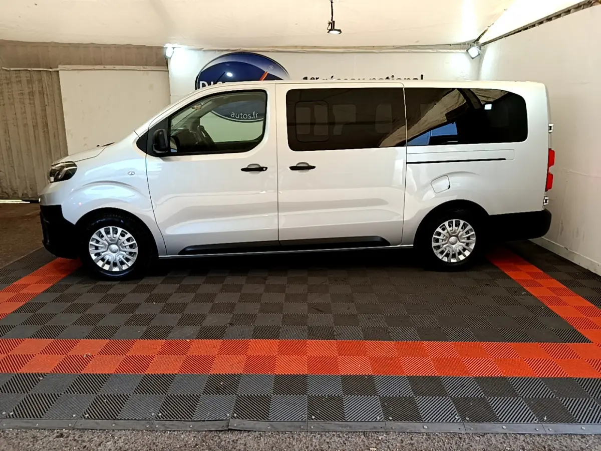 Profil côté gauche d'un Toyota Proace Verso gris clair avec vitres arrière teintées dans un garage.