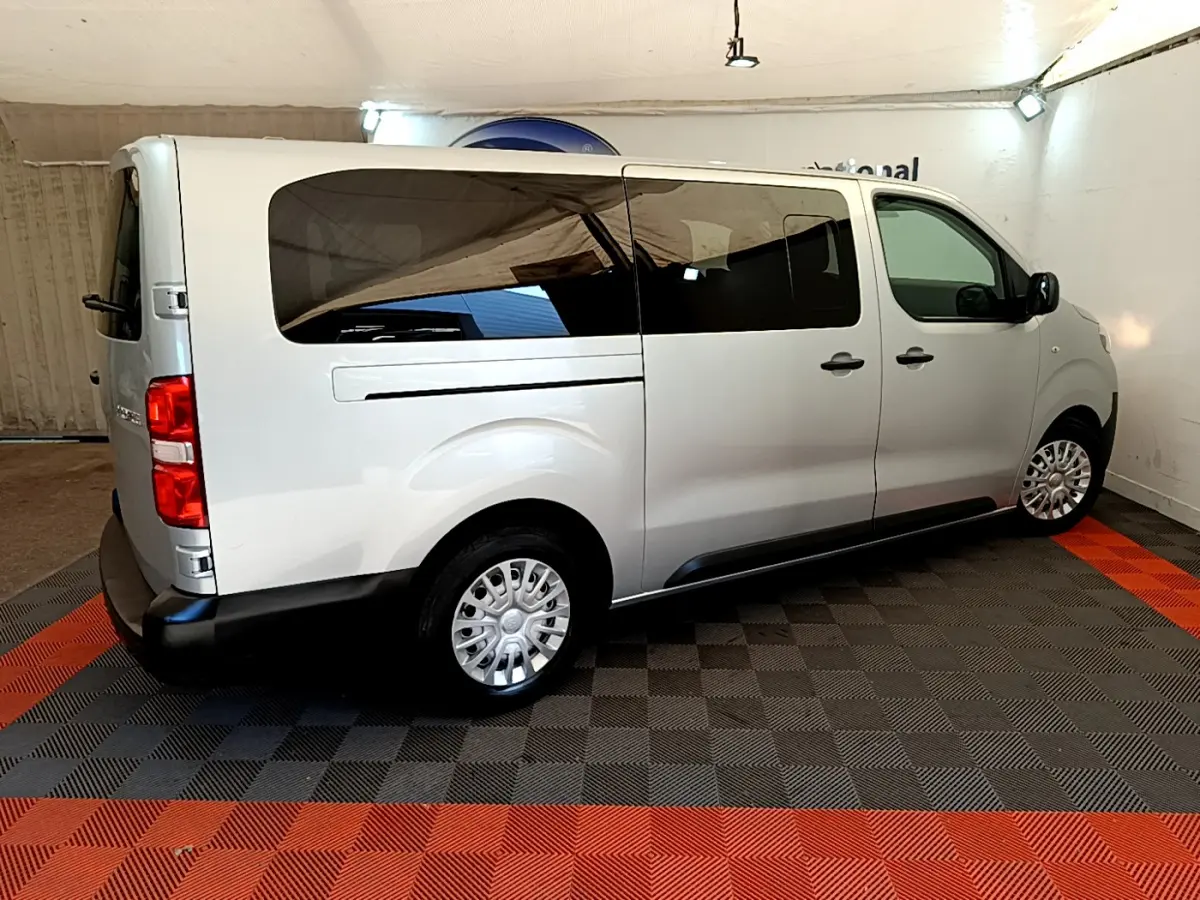 Vue 3/4 arrière droite d'un Toyota Proace Verso gris clair avec vitres teintées et jantes acier en intérieur showroom.