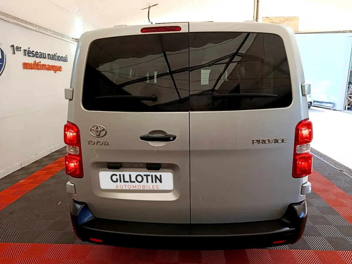 Vue arrière d'un Toyota Proace Verso gris clair avec portes vitrées teintées et feux rouges allumés en intérieur showroom.