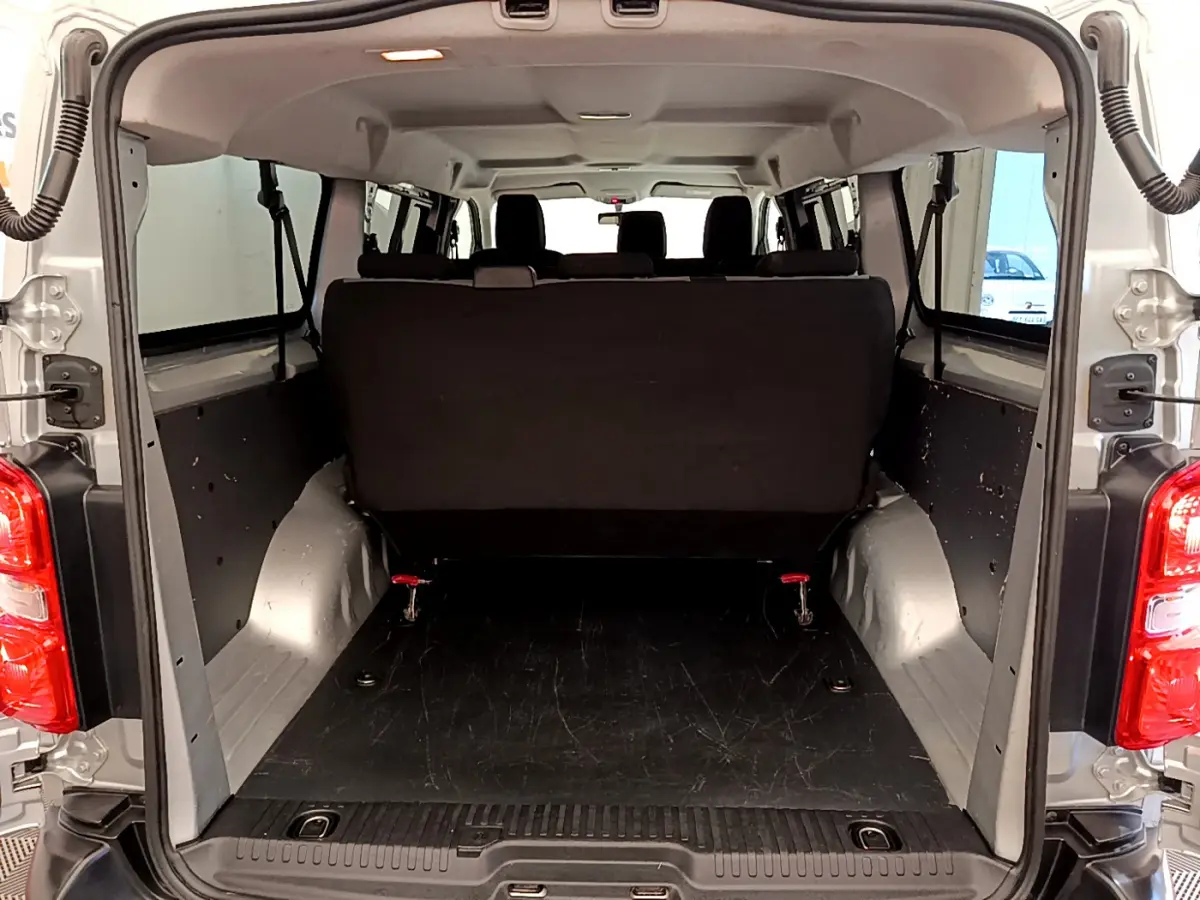 Vue arrière du coffre ouvert d'un Toyota Proace Verso gris clair, montrant l'espace de chargement et la banquette arrière noire.