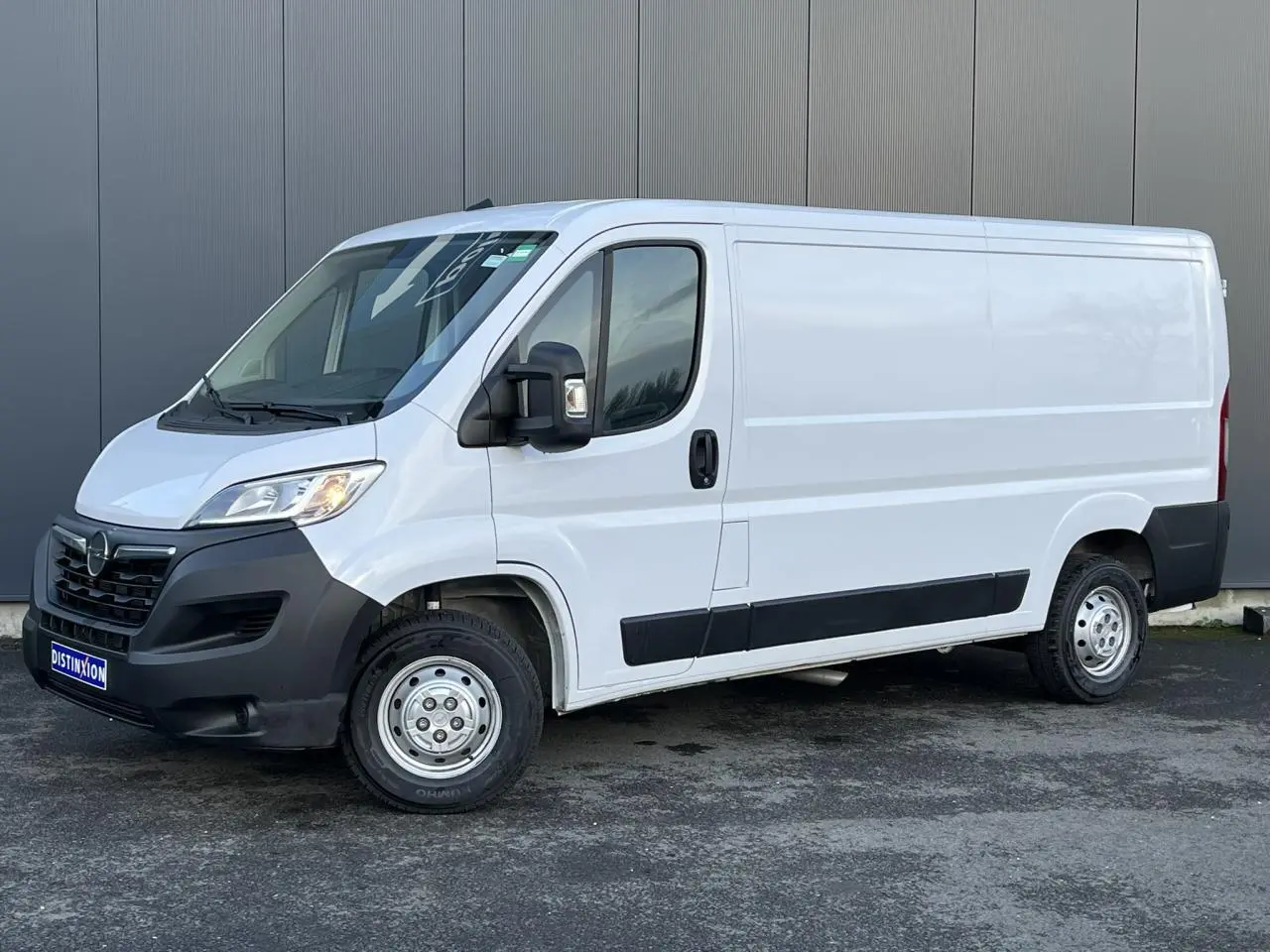 Vue 3/4 avant droit d’un Opel Movano Fourgon blanc 2024 avec pare-chocs noirs et rétroviseurs électriques rabattables.