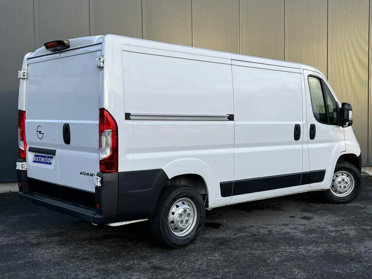Vue 3/4 arrière droite d'un Opel Movano Fourgon blanc avec porte latérale coulissante et protections noires.
