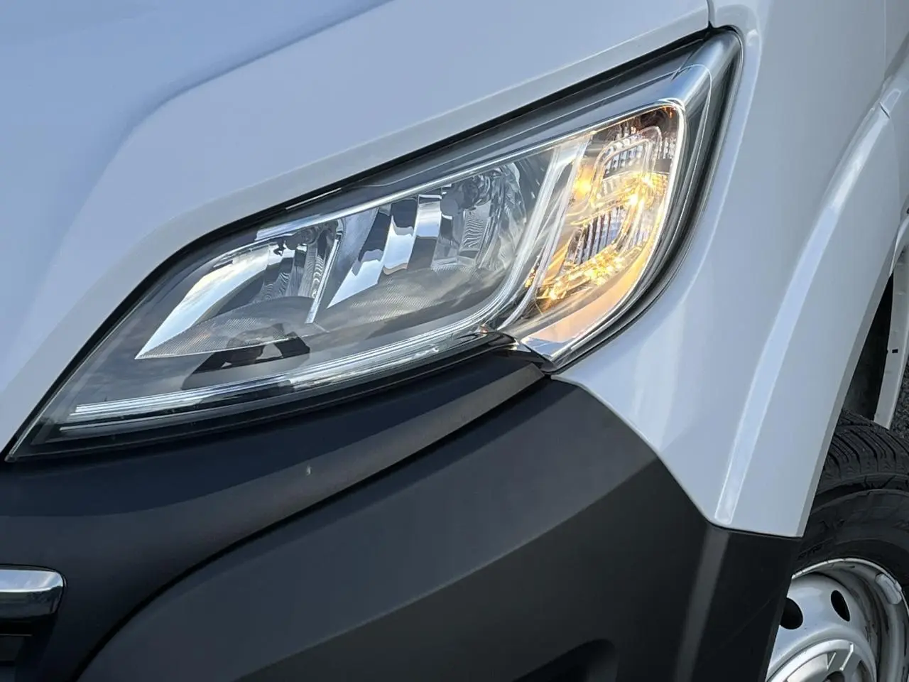 Gros plan sur le phare avant droit du fourgon blanc Opel Movano 2024 avec pare-chocs noir et roue acier visible.