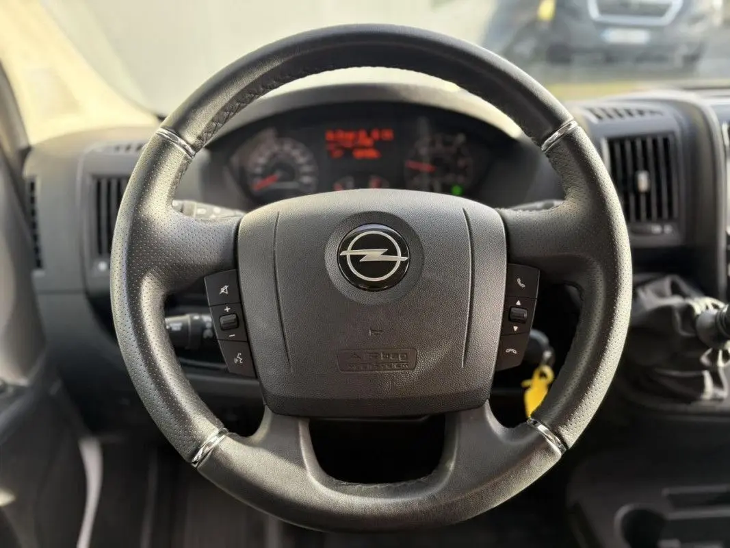 Vue rapprochée du volant noir de l’Opel Movano Fourgon 2023, avec commandes intégrées et tableau de bord en arrière-plan flou.