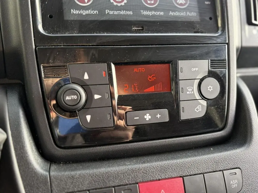 Gros plan sur la console centrale noire du tableau de bord de l’Opel Movano Fourgon blanc, affichant la climatisation automatique à 21°C.