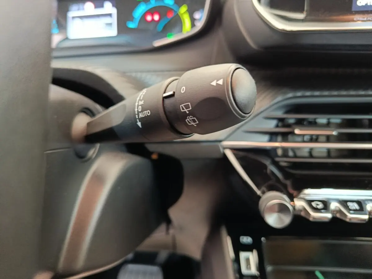 Gros plan sur la commande d’essuie-glace à gauche du volant dans l’habitacle d’une Peugeot 208 électrique blanche.