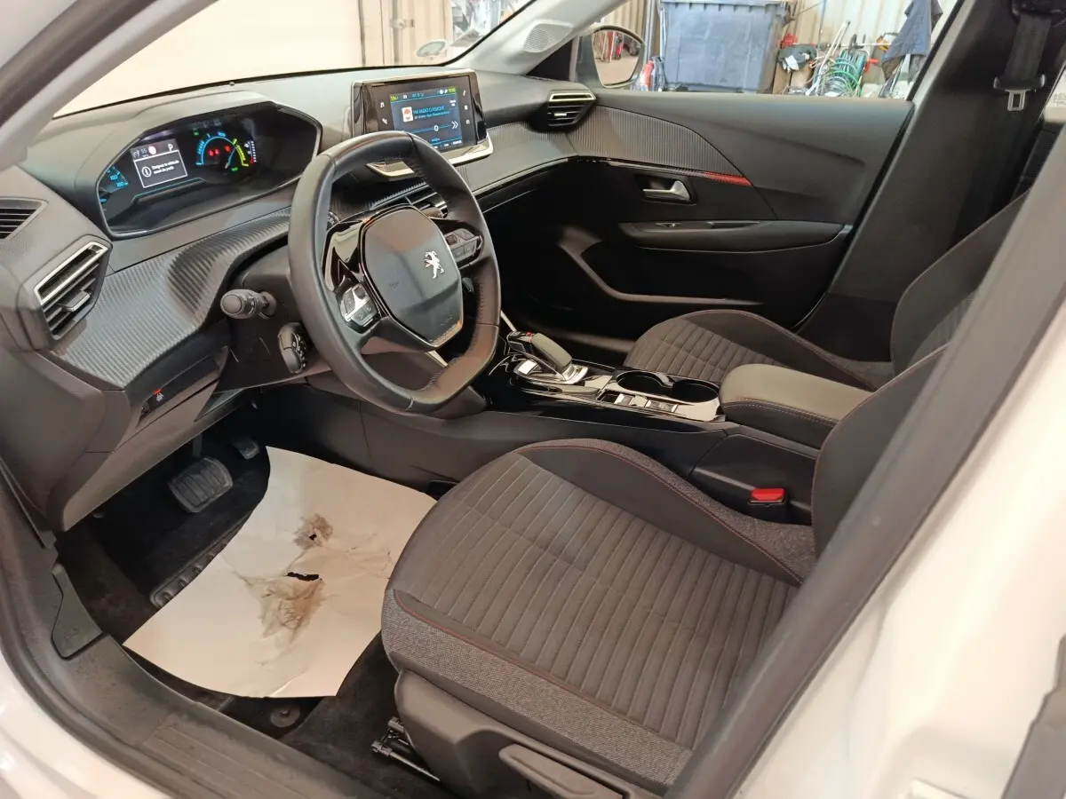 Intérieur avant droit de la Peugeot 208 électrique blanche, volant cuir, tableau de bord numérique et écran tactile central.