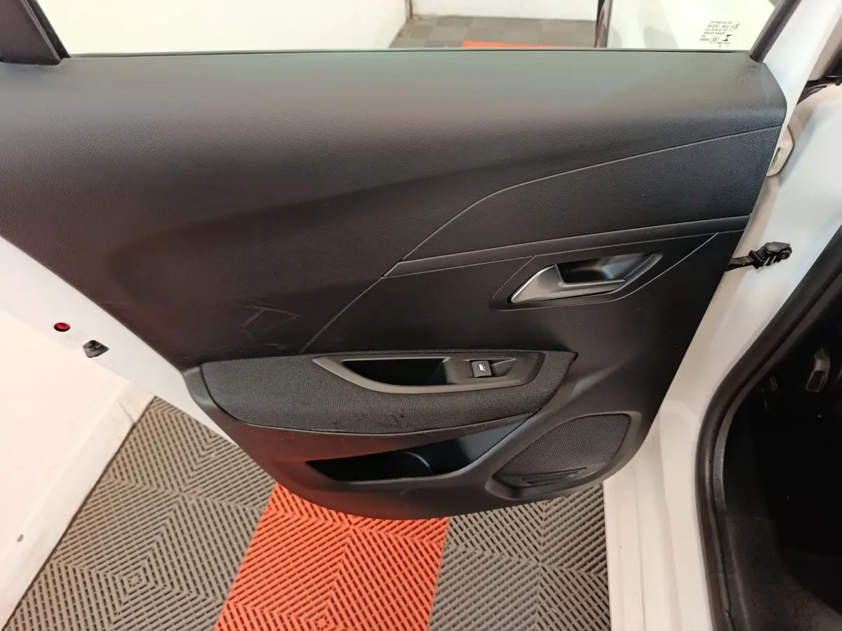 Vue intérieure de la porte arrière droite noire d'une Peugeot 208 électrique blanche, avec bouton de lève-vitre.