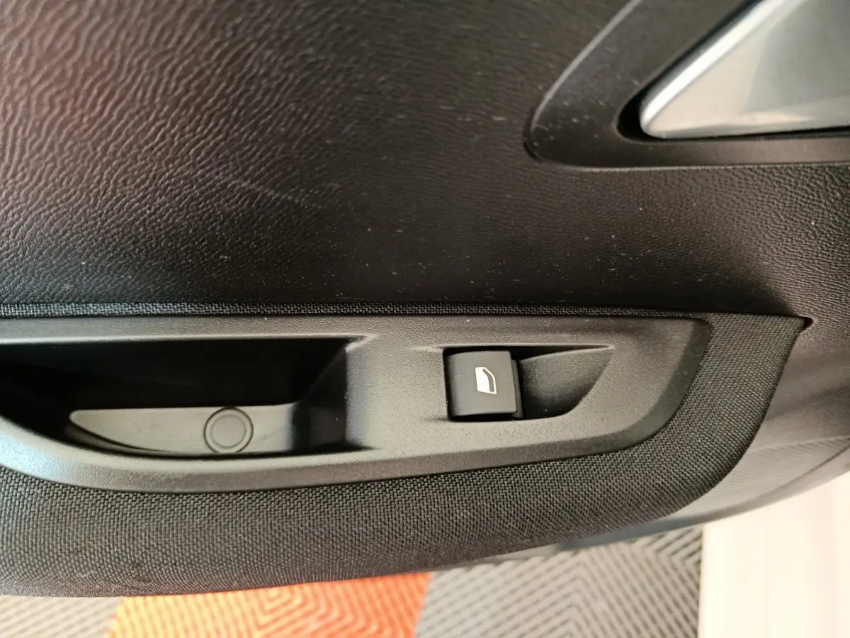 Gros plan sur la commande de lève-vitre électrique côté conducteur de la porte intérieure noire du Peugeot 208 électrique blanc.