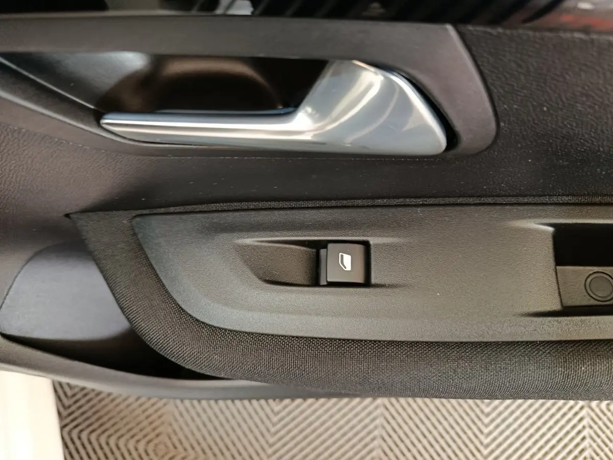 Détail de la poignée intérieure et bouton de lève-vitre côté conducteur d'une Peugeot 208 électrique blanche, vue rapprochée.