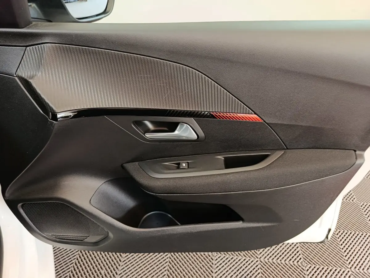 Vue intérieure côté gauche de la porte avant d’une Peugeot 208 électrique blanche avec insert décoratif noir et rouge.