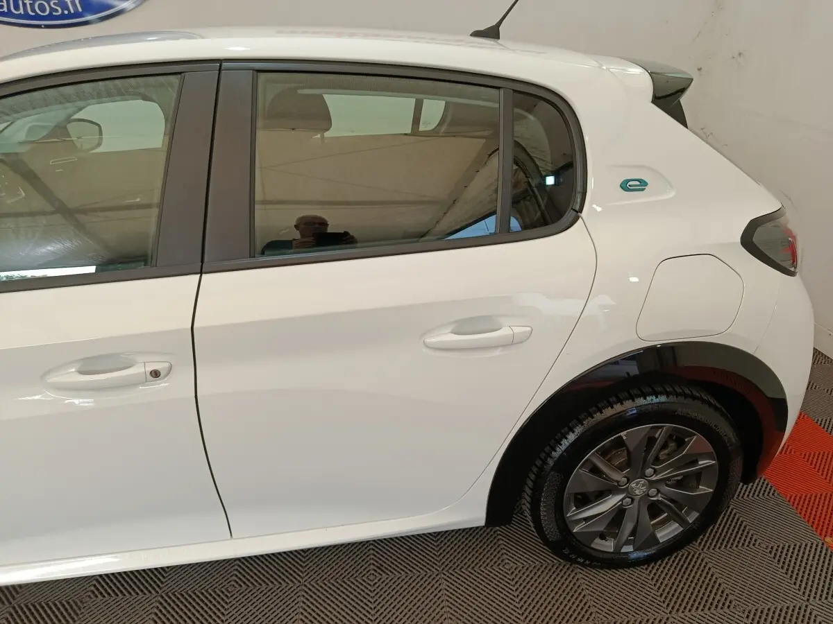 Vue latérale droite d'une Peugeot 208 électrique blanche, avec logo "e" distinctif sur l'aile arrière.