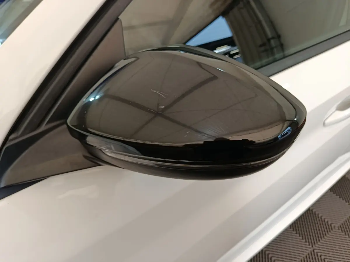 Rétroviseur noir brillant côté conducteur d’une Peugeot 208 électrique blanche vue en gros plan.