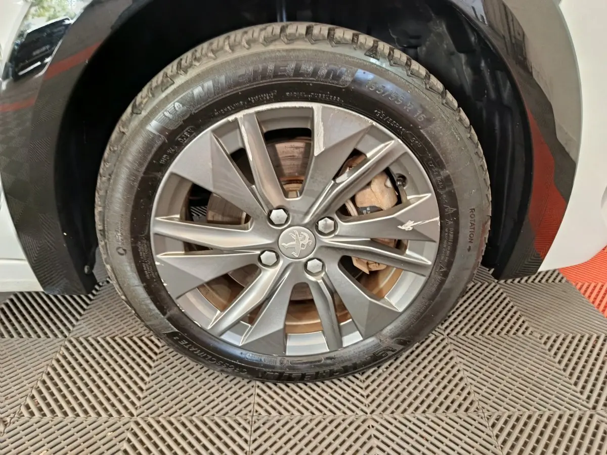 Gros plan sur la roue avant droite d'une Peugeot 208 électrique blanche avec jante alliage grise et logo lion central.